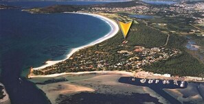 Vue aérienne d’une zone côtière comprenant une plage, une petite île avec des bâtiments et un port de plaisance avec des bateaux.