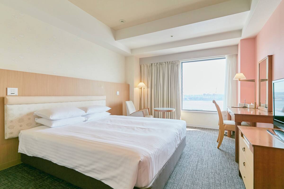 Habitación de hotel con una cama grande, un escritorio, una silla, una mesita y una ventana con cortinas.