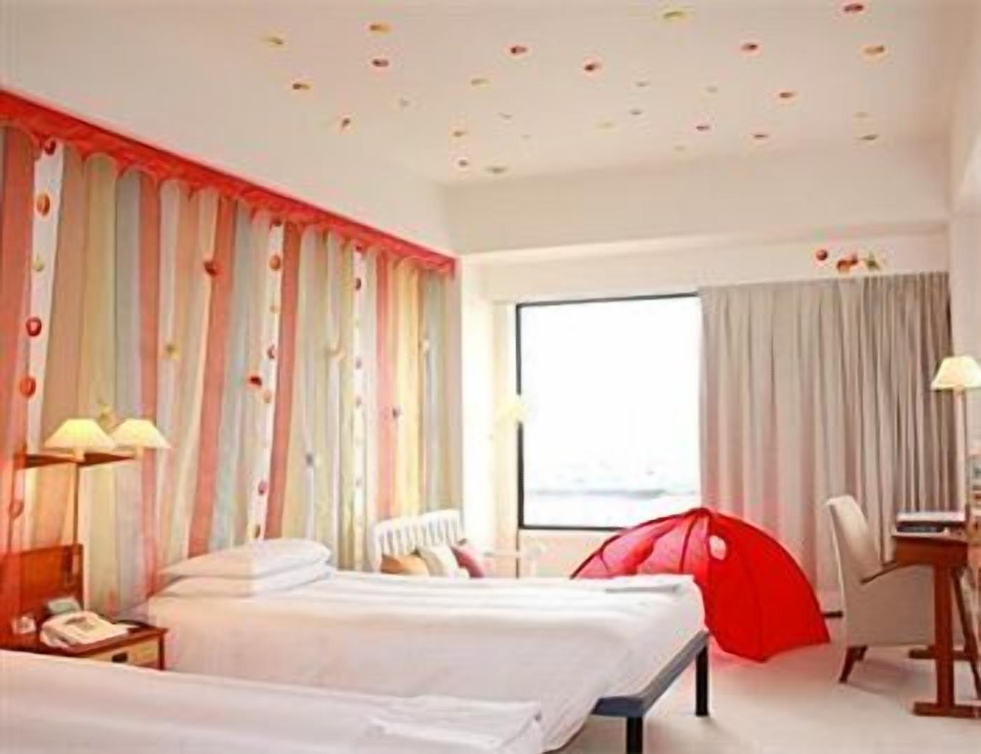 A hotel room with two beds, a desk, a chair, and a large window.