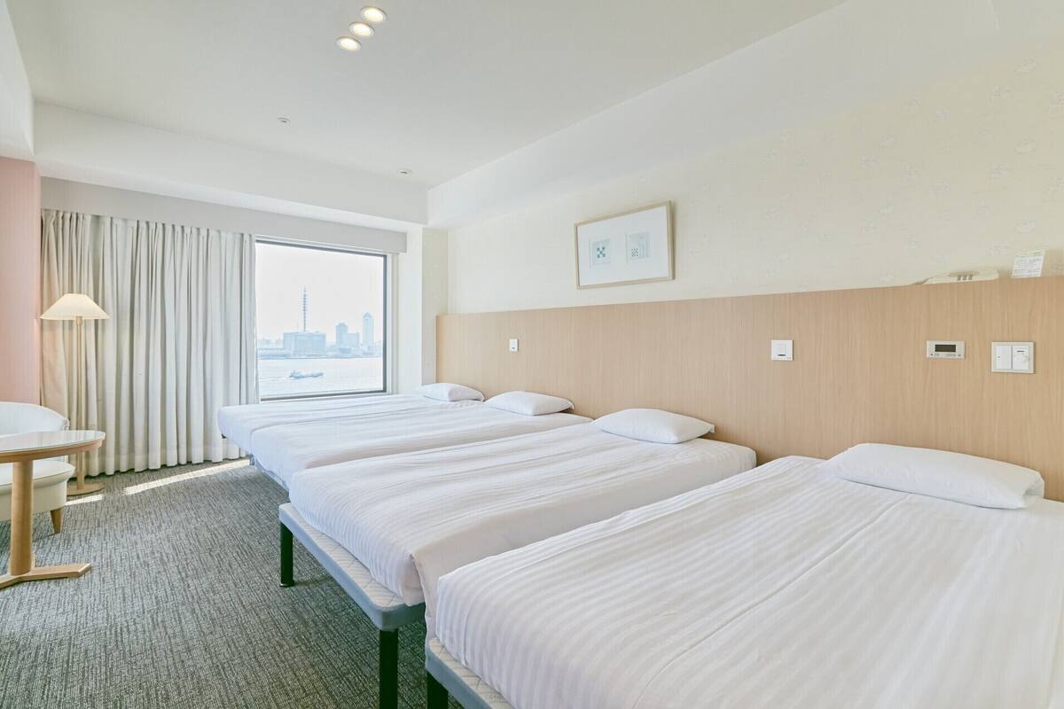 Habitación de hotel con tres camas, un escritorio y una ventana con vista a la ciudad.