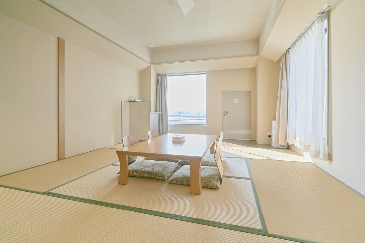 Una habitación tradicional japonesa con tatami, una mesa baja, cojines y vistas de la ciudad a través de la ventana.