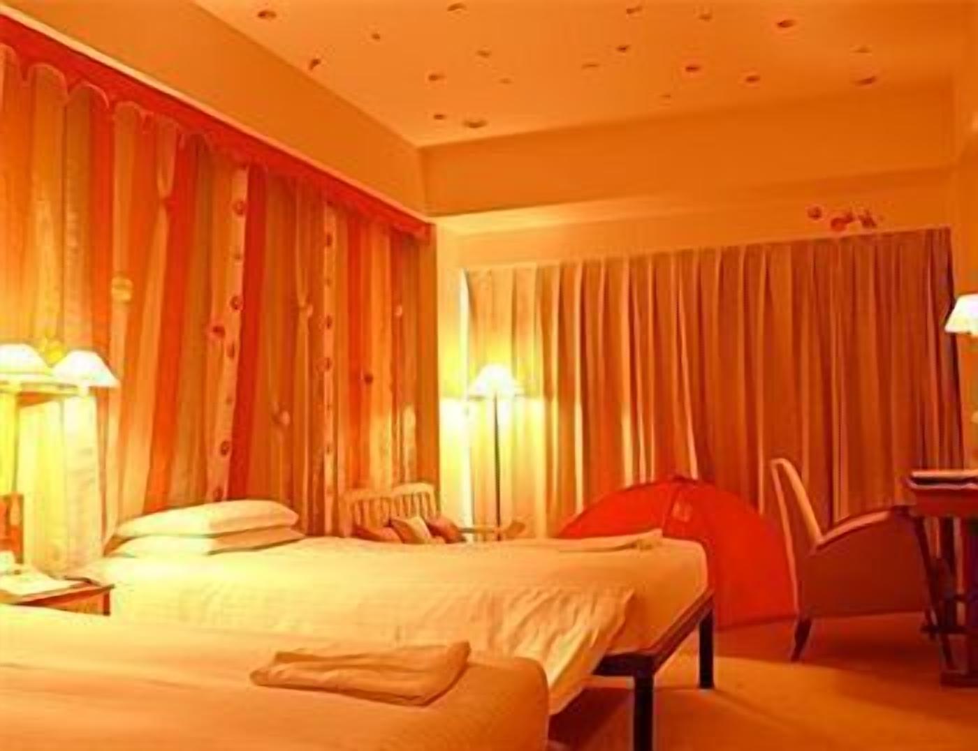 A hotel room with a bed, a chair, and a desk with a lamp.
