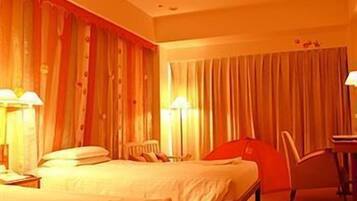 A hotel room with a bed, a chair, and a desk with a lamp.