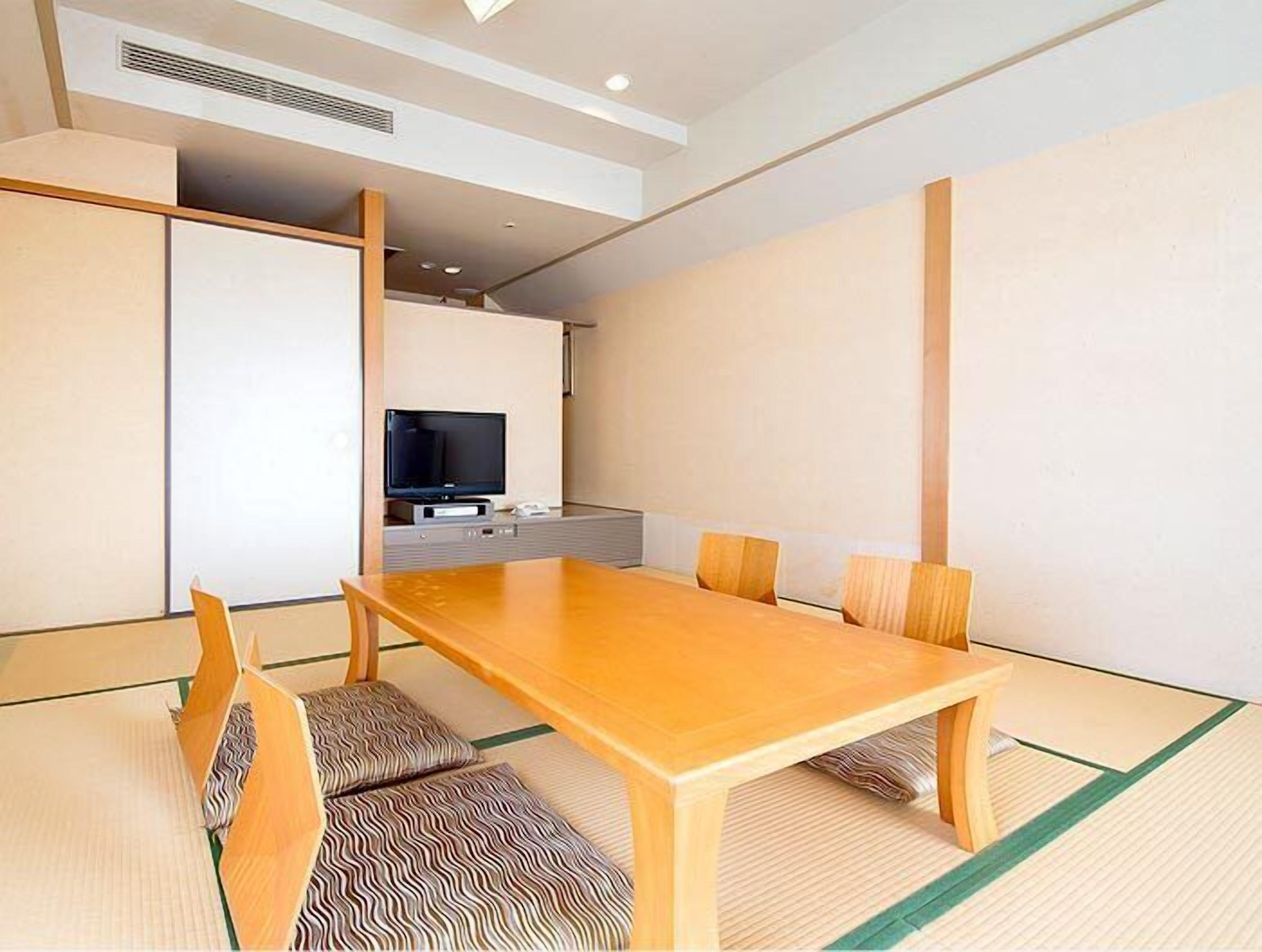 A traditional Japanese-style room with tatami flooring, a low wooden table, and a television in the background.