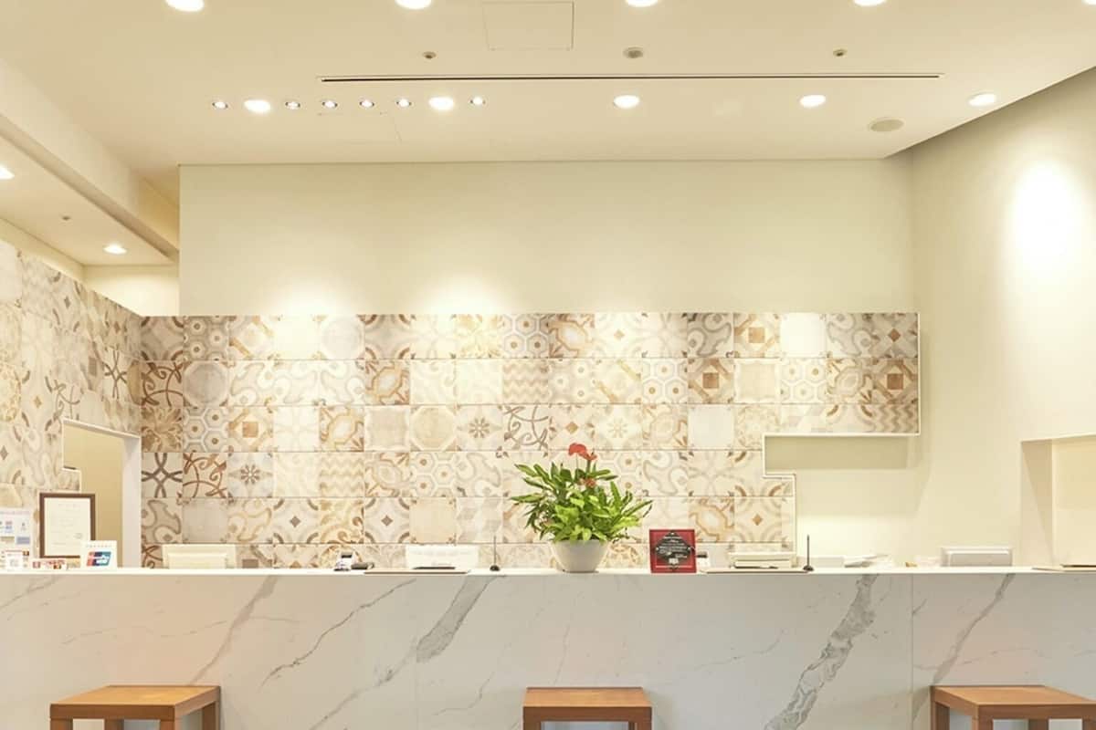 Una zona de recepción con mostrador de mármol, tres taburetes de madera, una planta en maceta y piso con diseño.