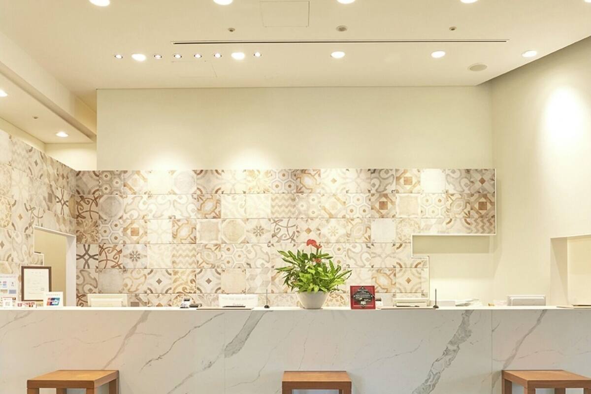 Una zona de recepción con mostrador de mármol, tres taburetes de madera, una planta en maceta y piso con diseño.
