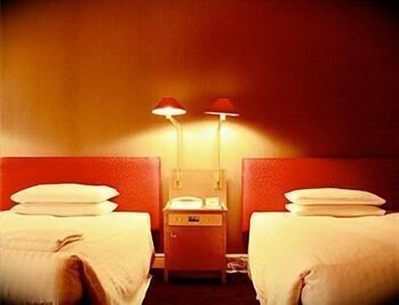 A hotel room with two beds, a nightstand, and two lamps.