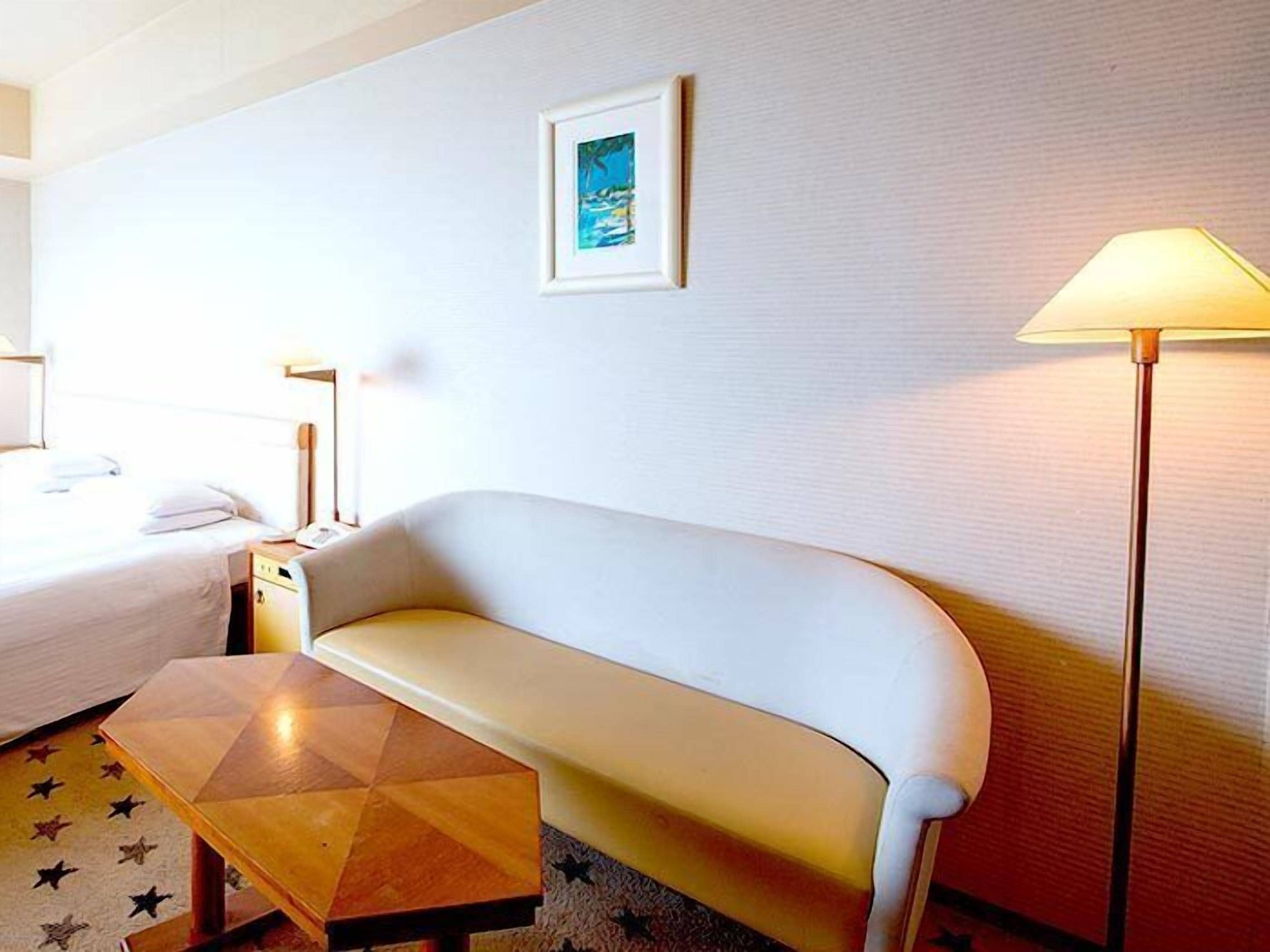 A hotel room with a white sofa, a wooden coffee table, a lamp, and a framed picture on the wall.