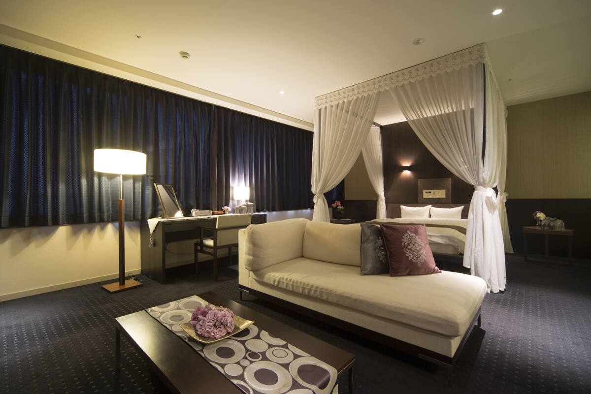 Una habitación de hotel con cama, sofá, escritorio y lámpara.