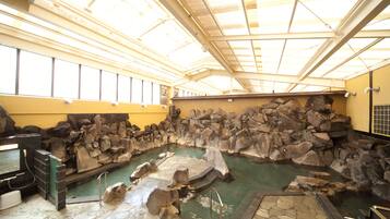 An indoor hot spring bath with a stone wall and a skylight ceiling.