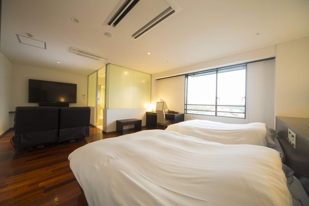 Una habitación de hotel moderna con una cama grande, un escritorio, una silla, un televisor y un ventanal amplio.