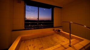 A wooden bathtub with a view of the city at dusk.