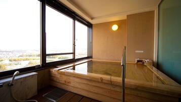 A wooden hot tub with a view of a cityscape through large windows.
