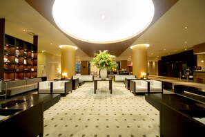 Relax in our stylish lobby, featuring a central seating area with sofas, armchairs, and a large table.