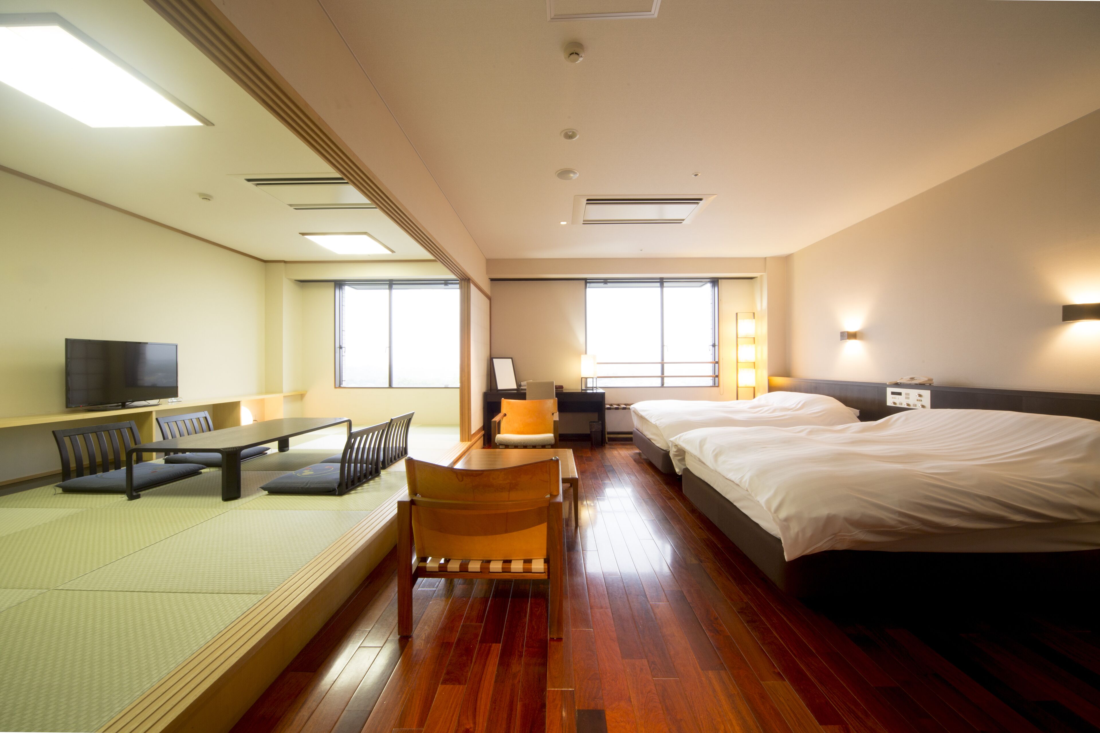 Habitación de hotel con piso de madera, una cama, un escritorio con silla, televisión y ventana.