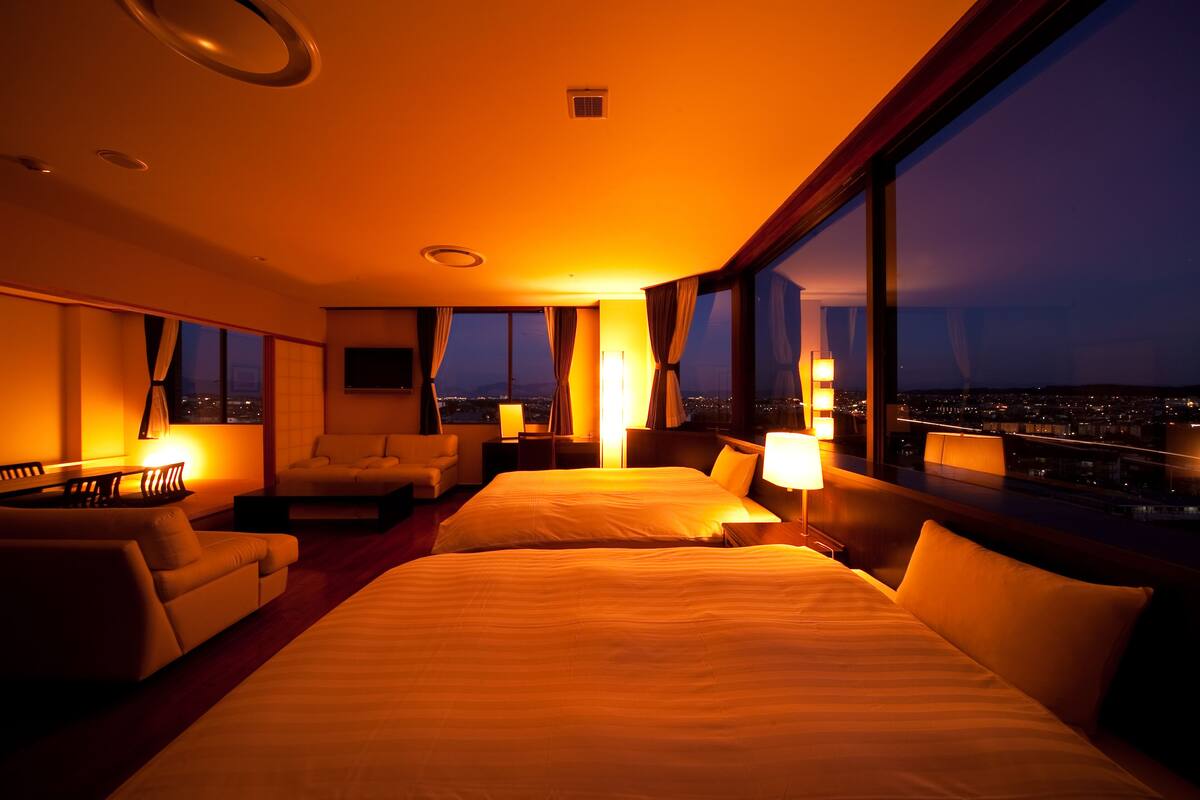 Habitación de hotel con dos camas, un sofá y vista a la ciudad de noche.
