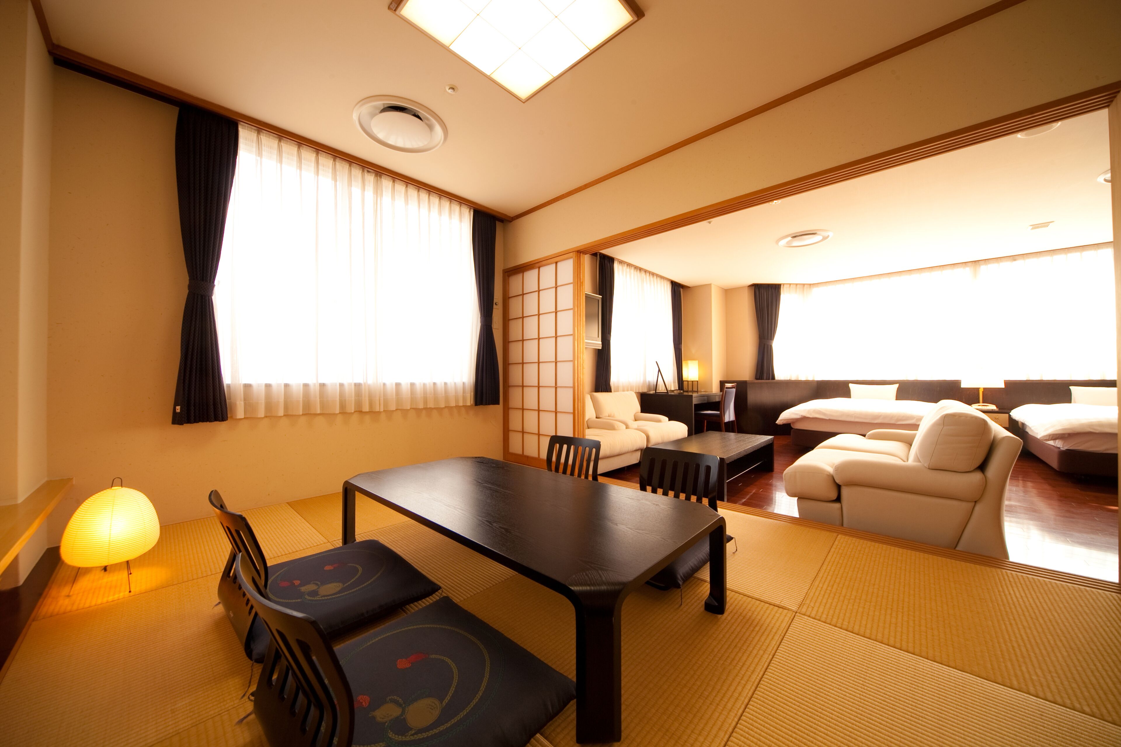 A traditional Japanese-style room with tatami flooring, a low table with cushions, a sofa, and a TV.