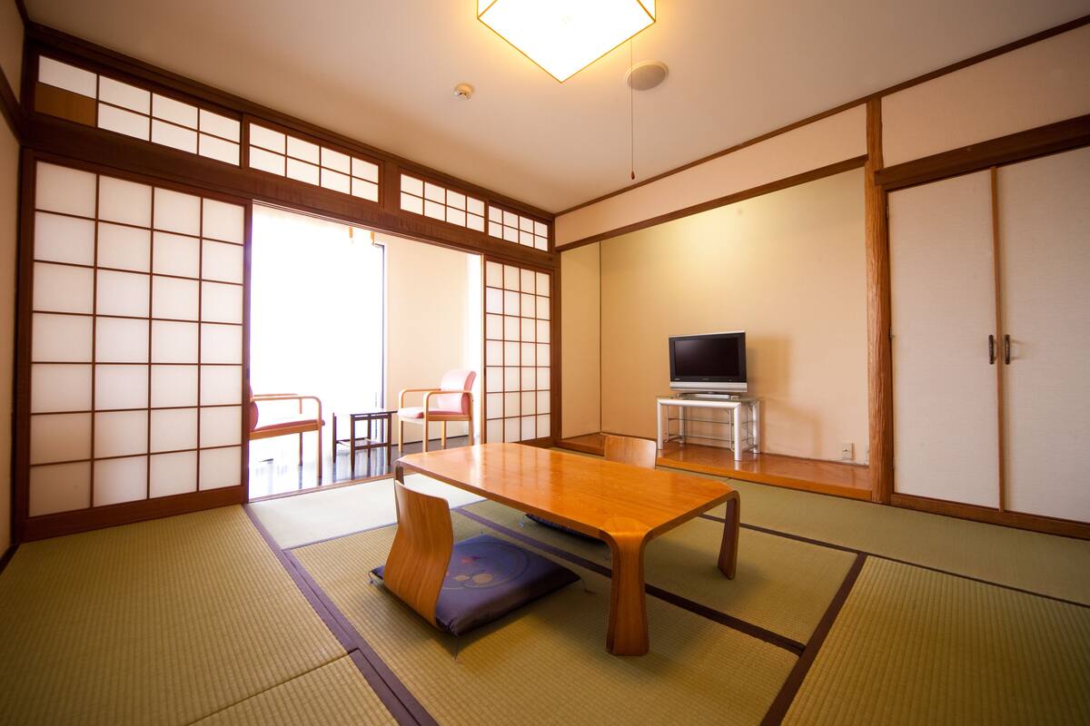Una habitación japonesa tradicional con suelo de tatami, una mesa de madera baja, un televisor sobre un mueble y puertas correderas.