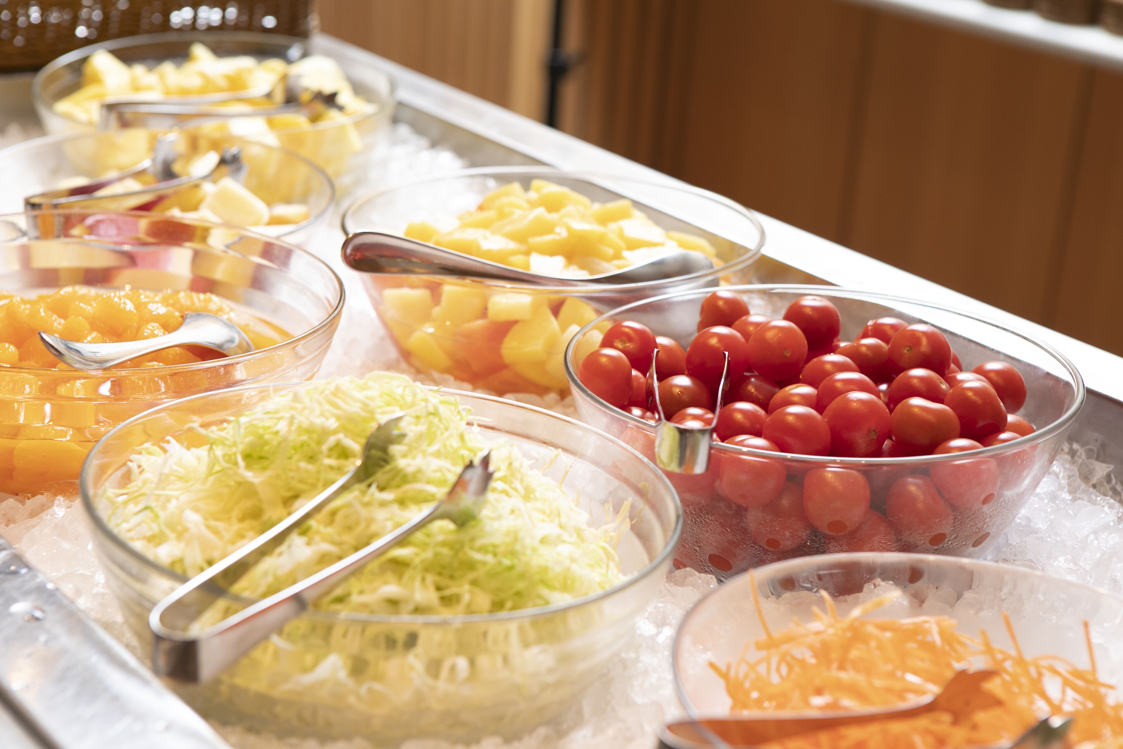 A buffet with various food options including fruits, vegetables, and shredded cheese.
