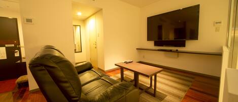 A modern living room with a leather sofa, a flat-screen TV mounted on the wall, and a small wooden table.