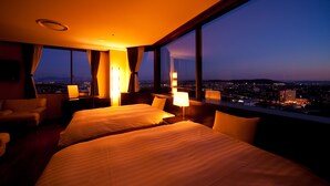 A hotel room with two beds, a view of the cityscape at dusk, and a large window with curtains.