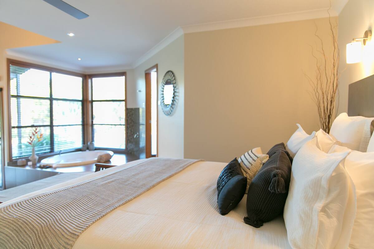 A modern hotel room with a large bed, a view of a spa area, and a large window.