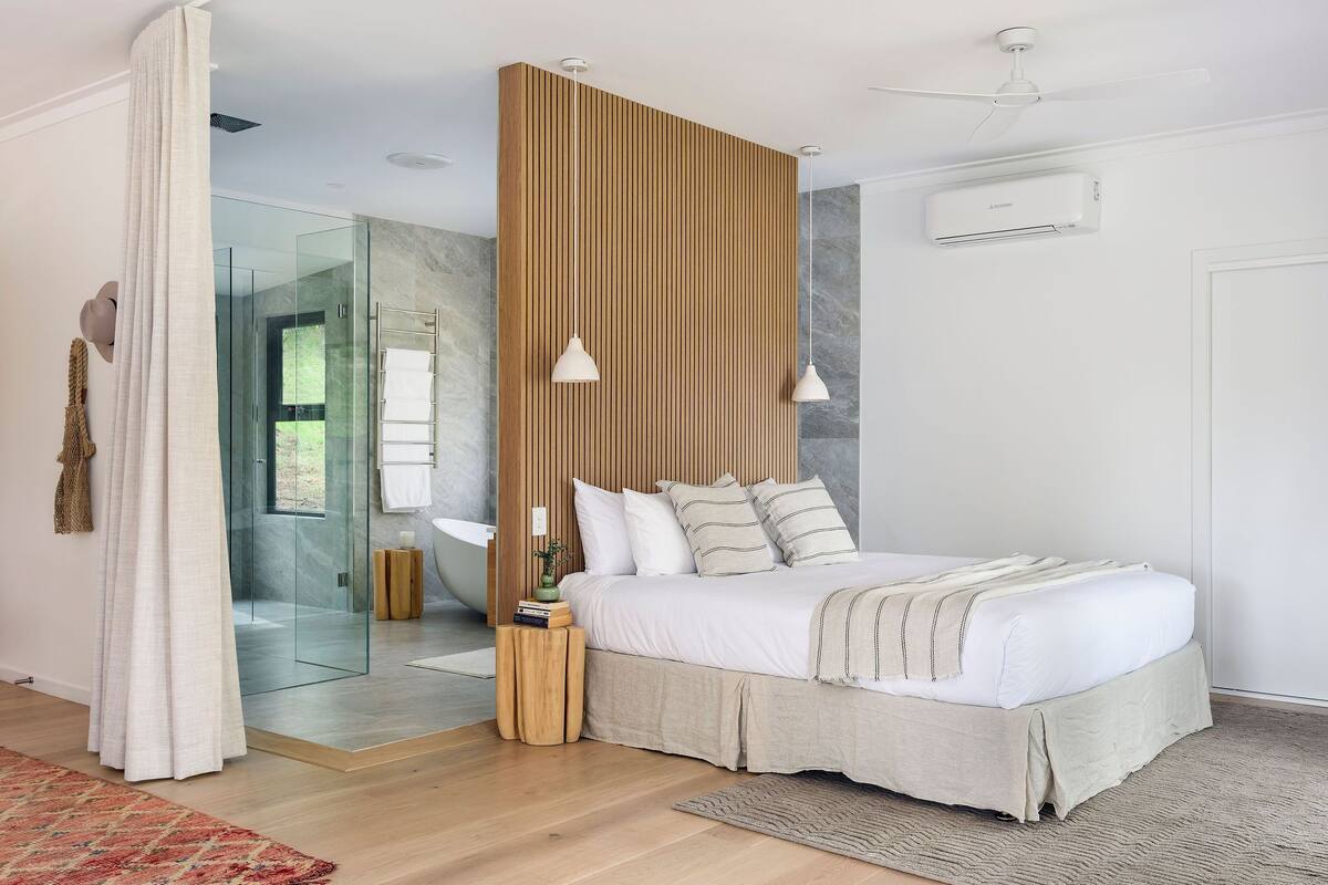 A modern bedroom with a large bed, wooden panel wall, and a glass shower area.