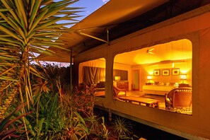 A room with a bed, a sofa, and a dining table. There is a window with curtains, and the room is lit by warm lighting. - The Billi Resort (Cable Beach)