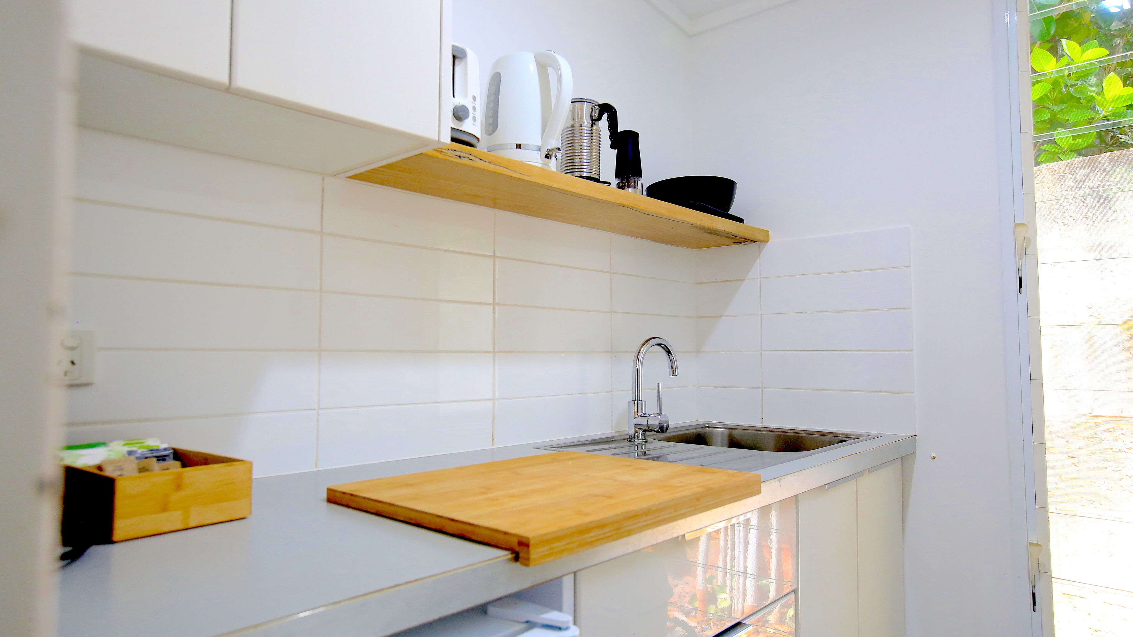 A kitchen with white tiles, a wooden countertop, a sink, and a shelf with kitchen appliances.