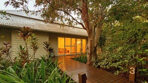 A house with a wooden deck, surrounded by lush greenery and a tree. - The Billi Resort (Cable Beach)