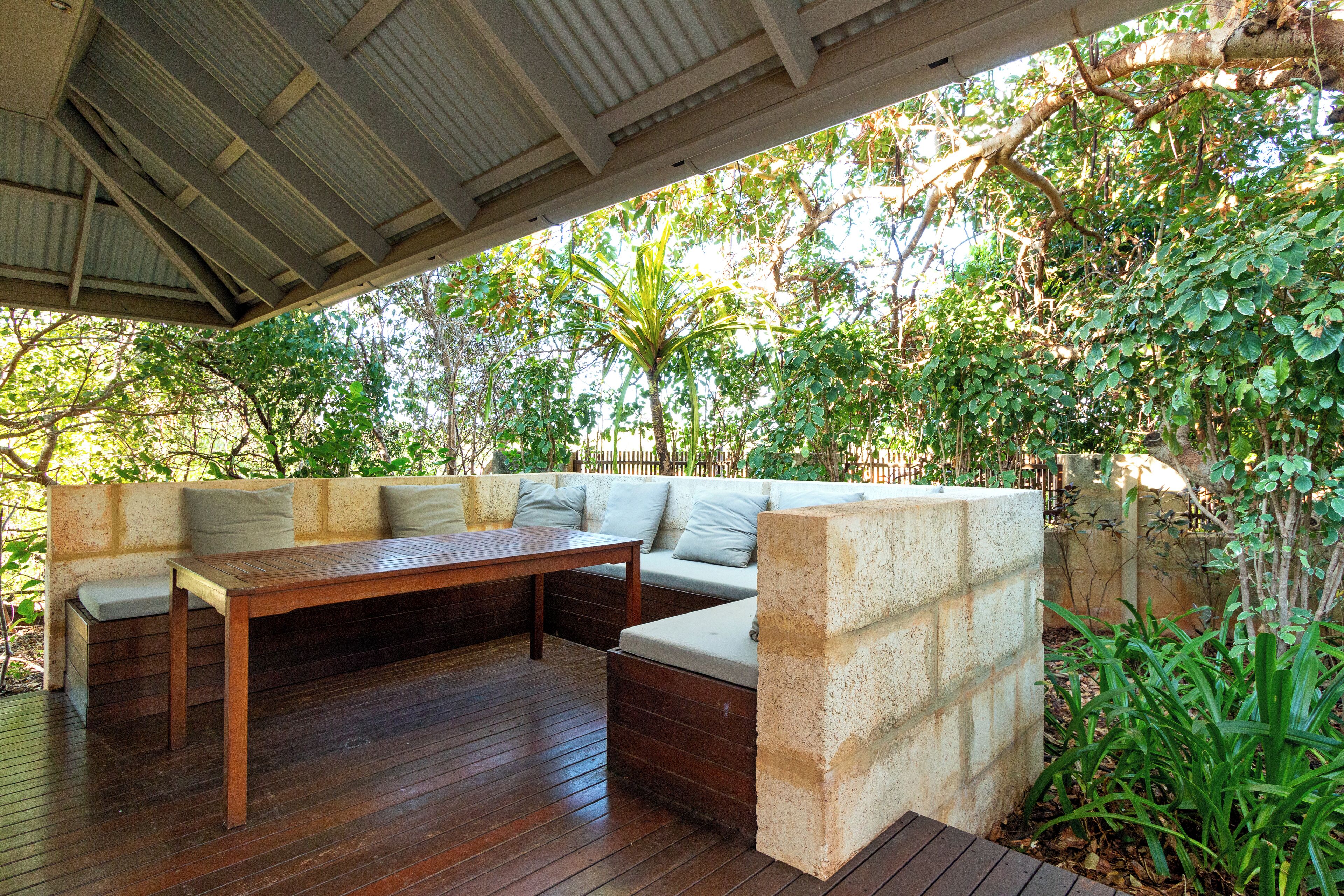 Un espace extérieur aménagé avec une table en bois et des bancs, entouré de verdure et d’un mur en pierre.