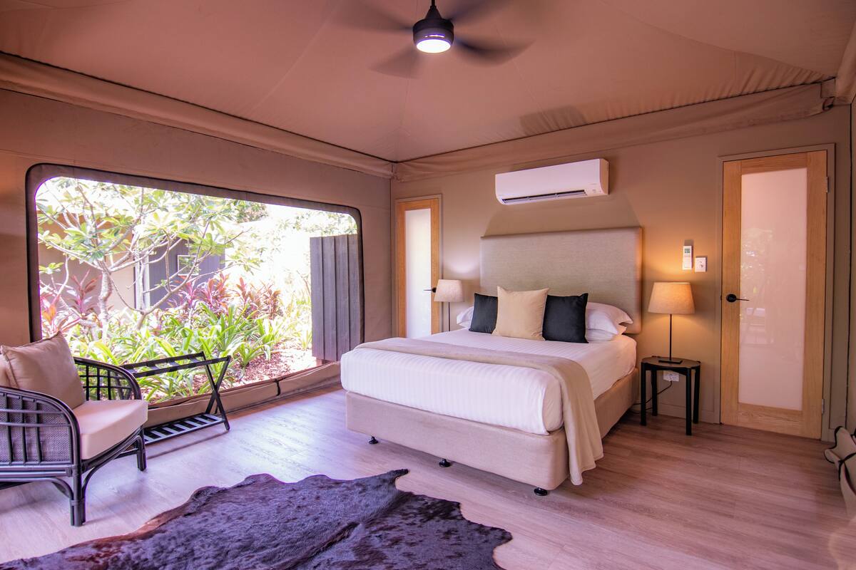 A bedroom with a large window, a bed, a chair, and a small table.