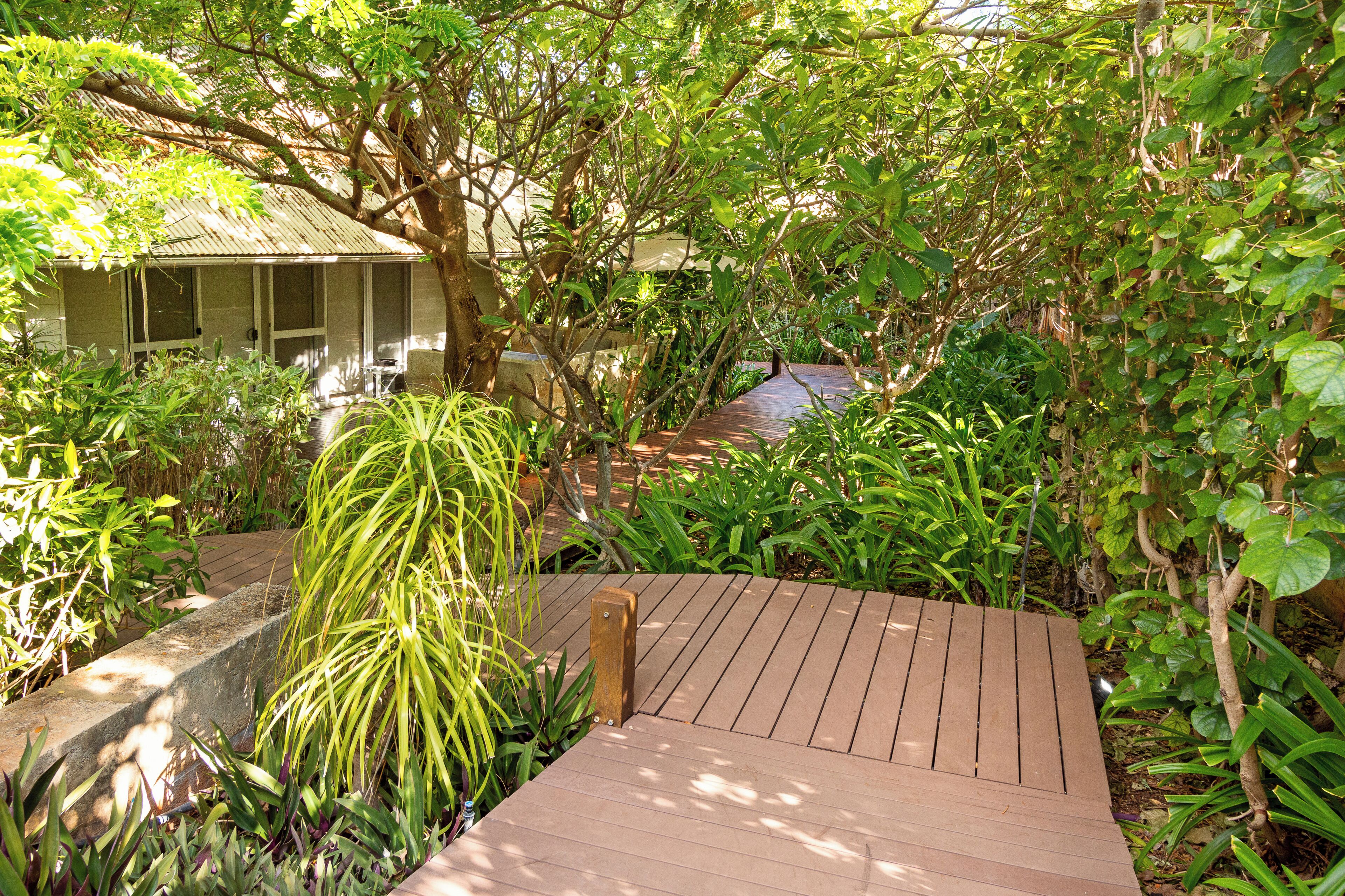 A wooden deck surrounded by lush greenery and a house with a sloped roof.