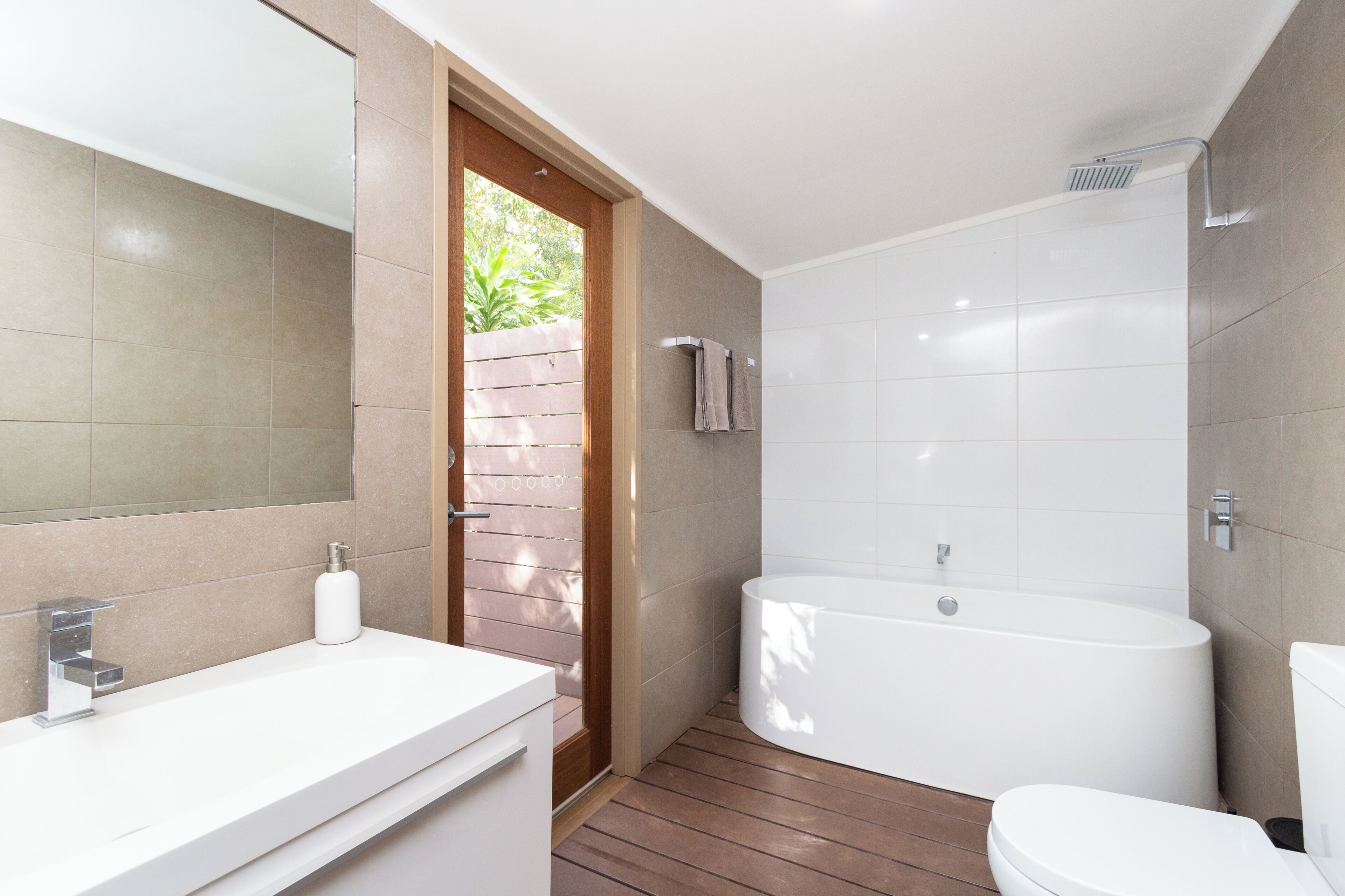 Un baño moderno con suelo de madera, una bañera blanca y un lavamanos blanco.