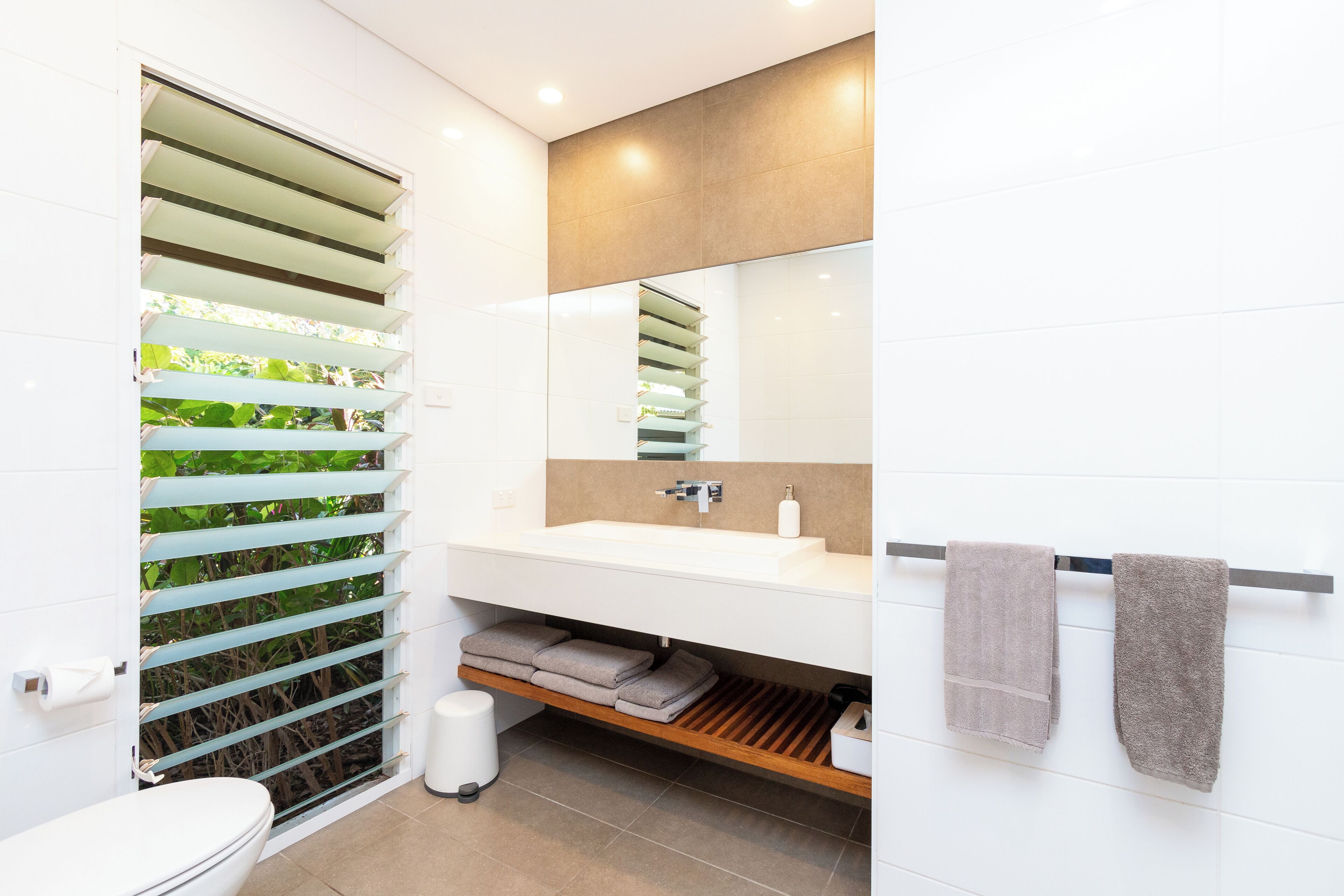 A modern bathroom with a white sink, mirror, and towel rack.