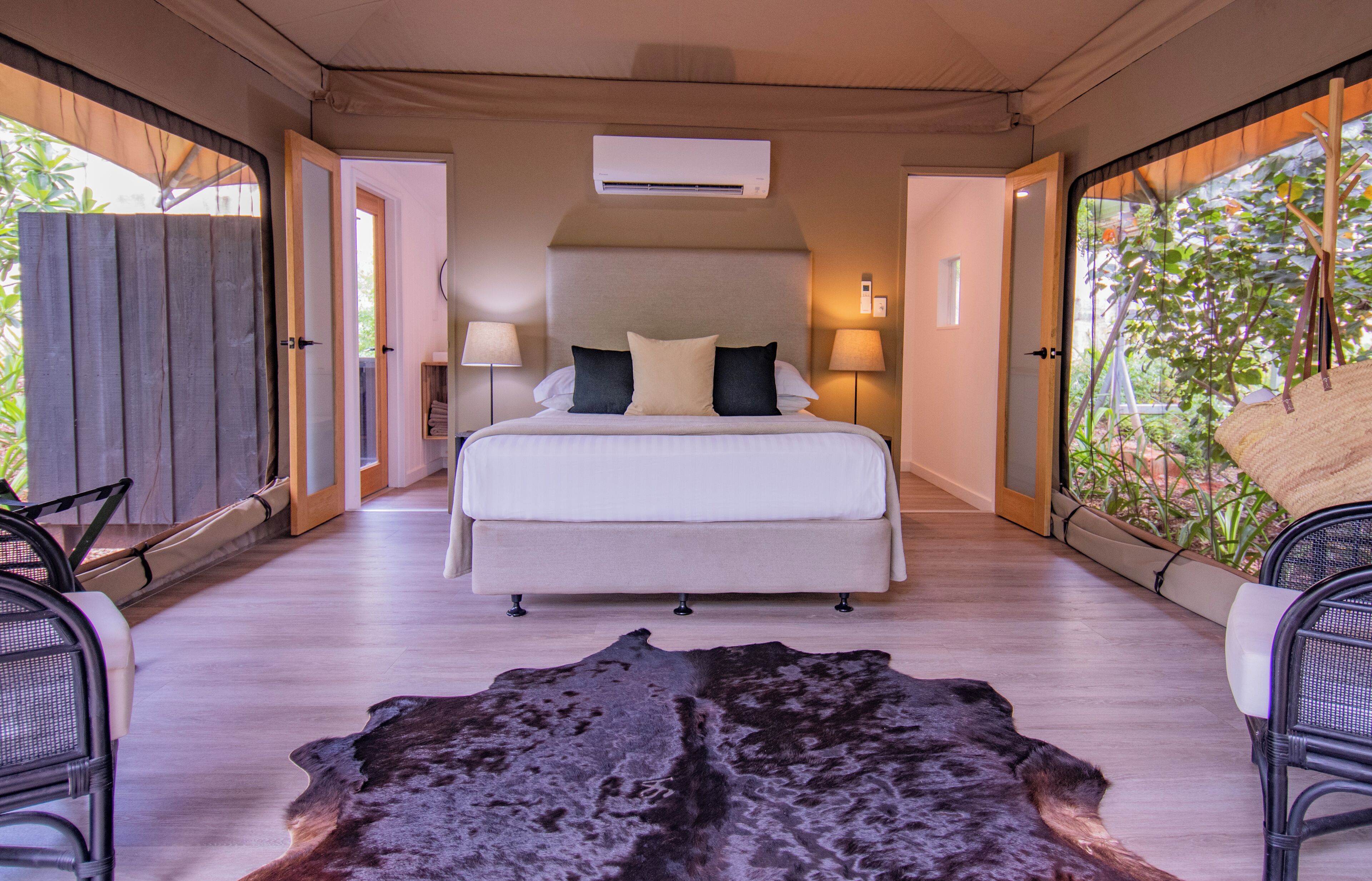 A spacious bedroom with a large bed, two bedside lamps, and an air conditioning unit.