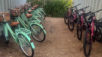 A row of bicycles parked on gravel, with a fence and greenery in the background.