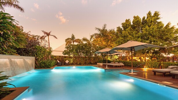 A swimming pool with lounge chairs and umbrellas, surrounded by lush greenery and trees. - The Billi Resort (Cable Beach)