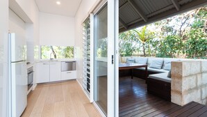 A modern kitchen with white cabinets and a sliding glass door leading to an outdoor seating area with a wooden deck and a stone wall. - The Billi Resort (Cable Beach)