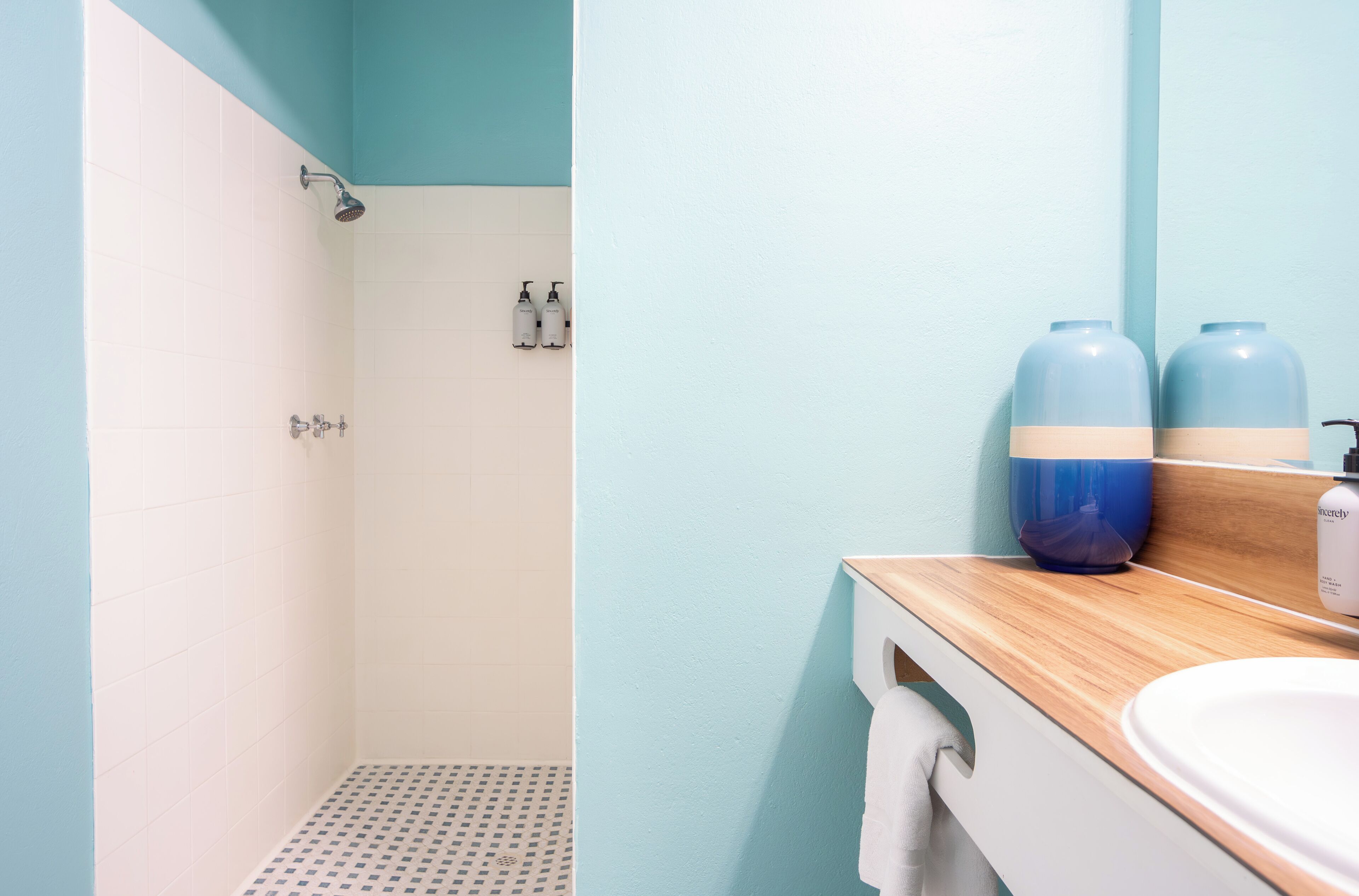 A bathroom with a shower, a sink, and two large blue containers on the countertop.
