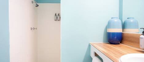 A bathroom with a shower, a sink, and two large blue containers on the countertop.