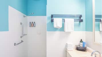 Un baño con ducha, lavabo y espejo. Hay toallas y artículos de aseo en el mostrador.