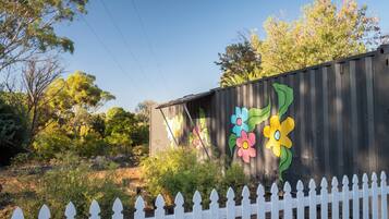 Surrounded by lush trees and vibrant artwork, this property features a charming picket fence and a repurposed shipping container.