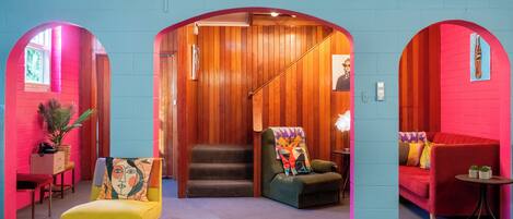 A brightly colored interior with a yellow armchair, a red sofa, and a staircase leading to a wooden loft area.