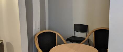 A small room with a round table and two chairs, a wardrobe, and a ceiling light.