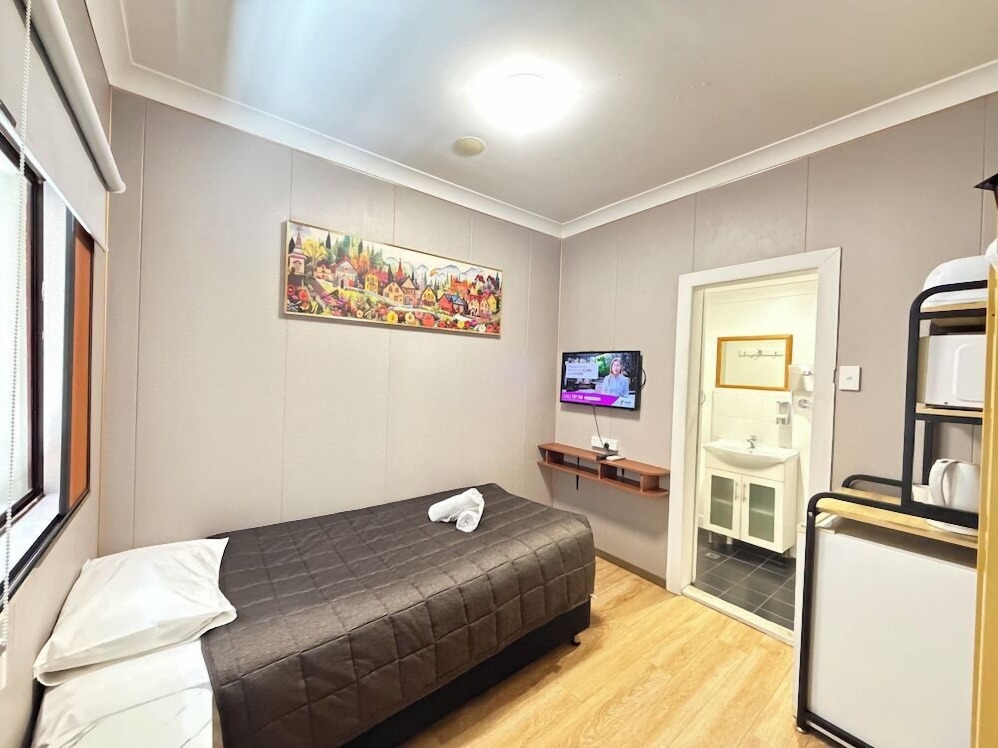 Un dormitorio con cama, televisión, un cuadro, un lavamanos y un mueble pequeño.
