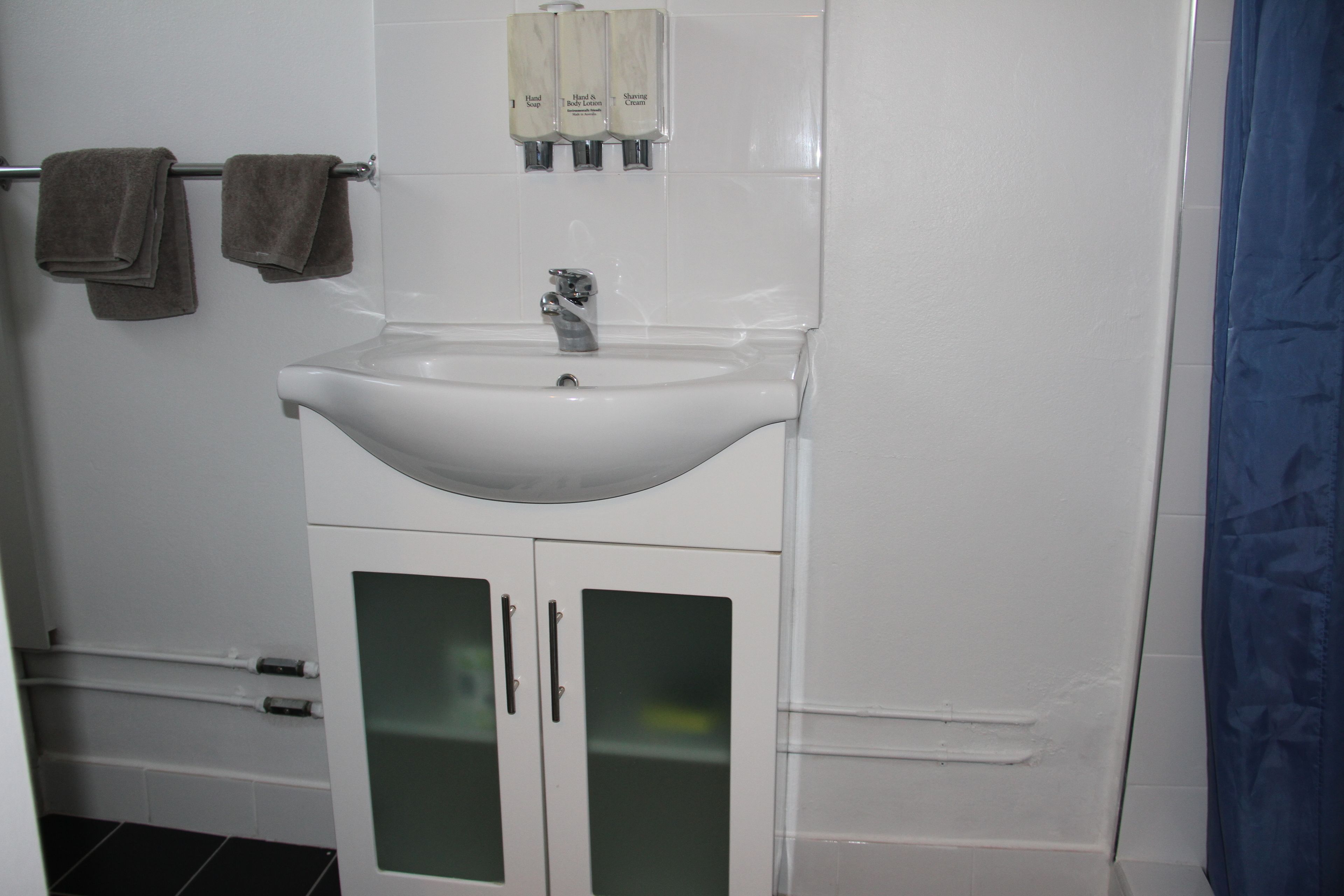 A bathroom with a white sink, two towels on a rack, and three soap dispensers.