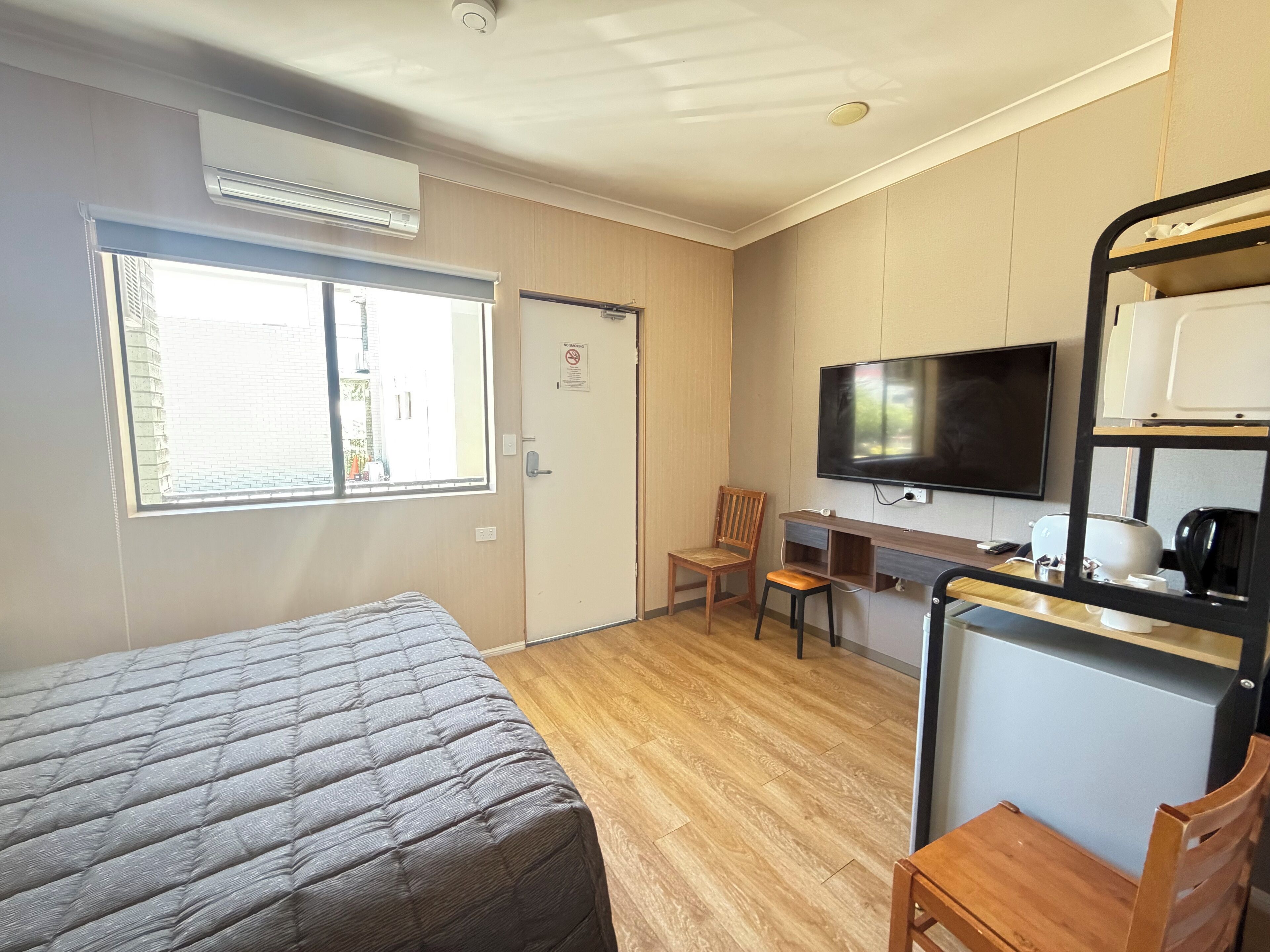 Habitación de hotel con cama, escritorio con silla, televisor y una zona de kitchenette.