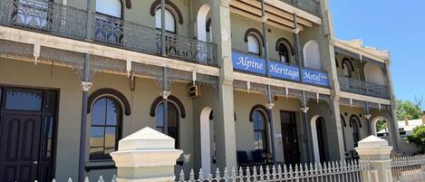 A building with a sign reading "Alpine Heritage Motel." It features multiple balconies with ornate railings and a gated entrance.