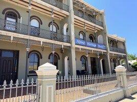 Un edificio con un letrero que dice "Alpine Heritage Motel". Cuenta con varios balcones con barandillas ornamentales y una entrada protegida por una reja.